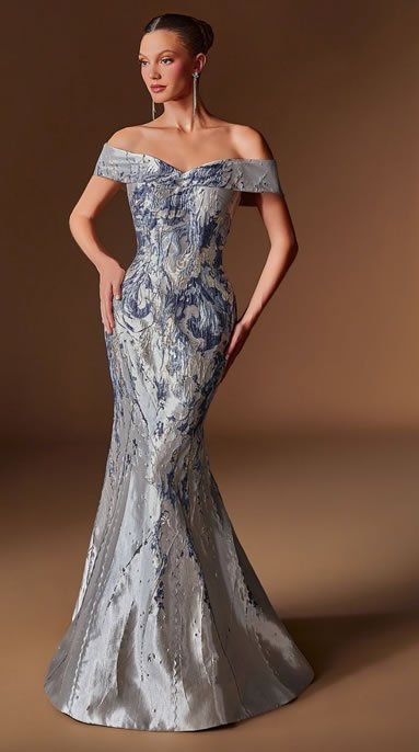 Off-shoulder silver-blue mermaid gown on a model, with a fitted bodice and train, posing against a brown backdrop.