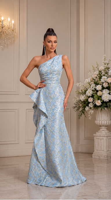 Woman in a light blue one-shoulder evening gown with a cascading ruffle, standing in an elegant room with a chandelier and flowers.