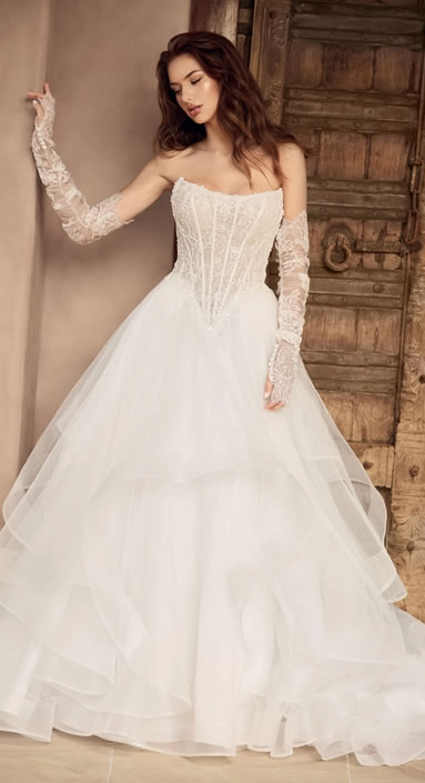 Bride in an off-shoulder lace wedding dress with a full layered tulle skirt, standing by a rustic wooden door.
